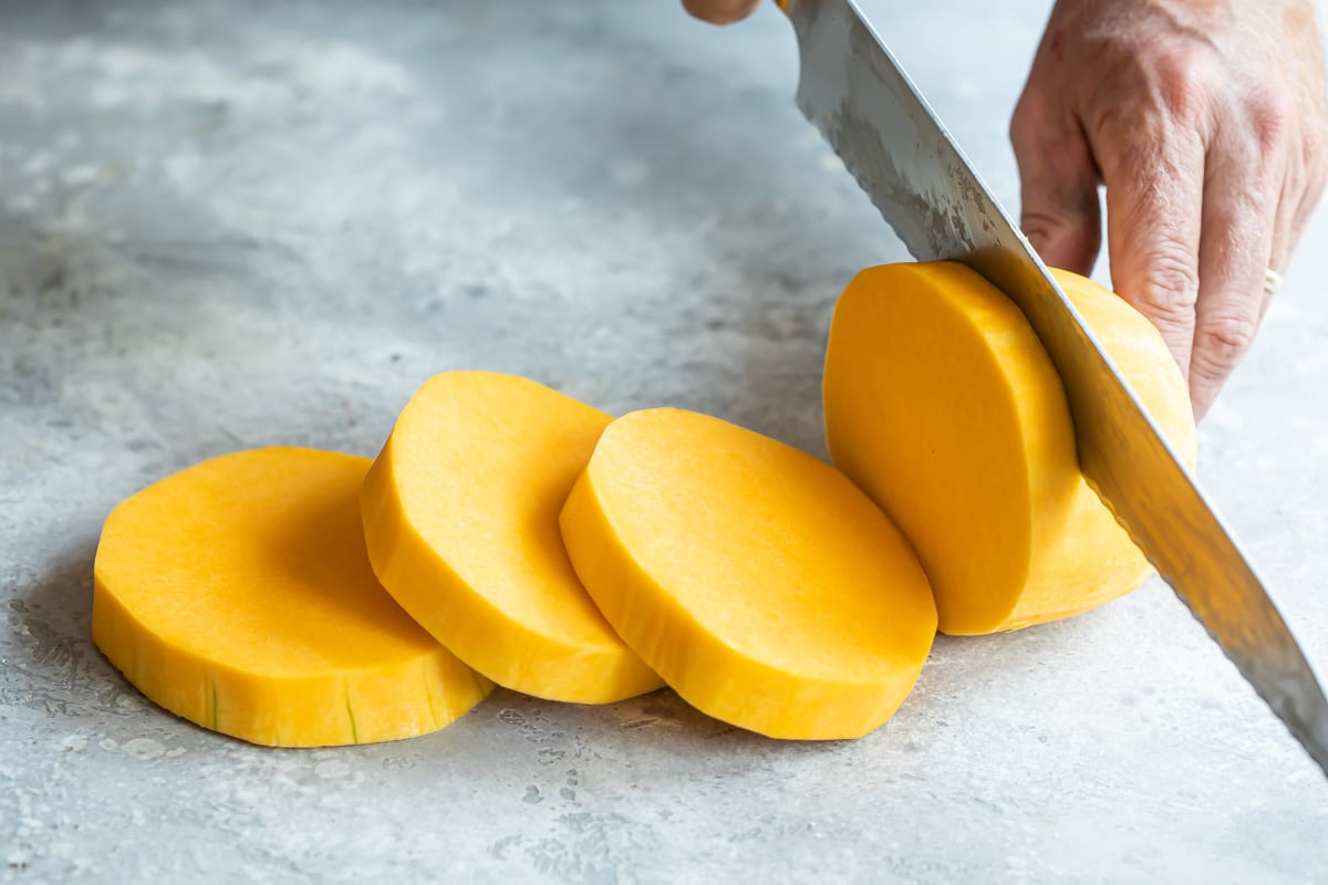 Peeled butternut squash being sliced into rounds.