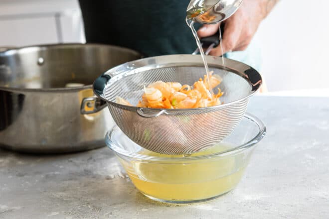 Shrimp stock being strained over a clear bowl.