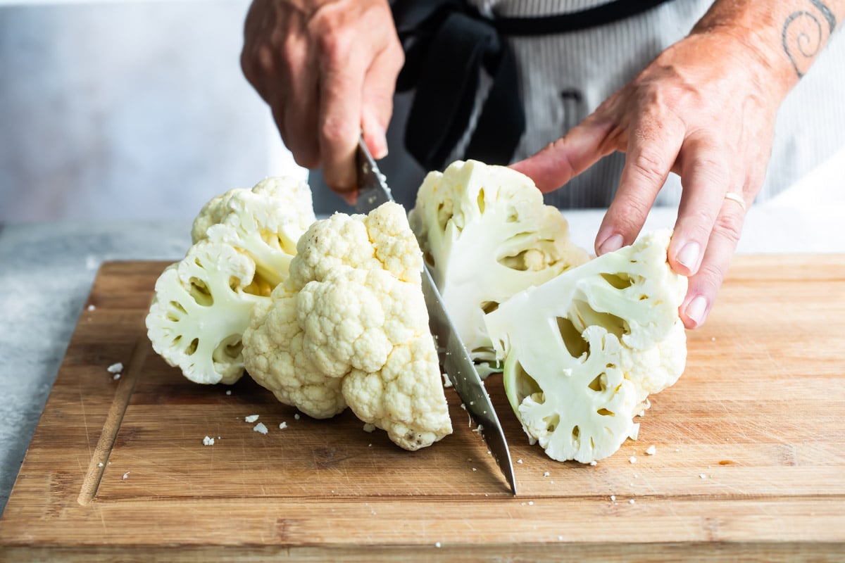 Raw cauliflower being chopped on a wooden cutting board.