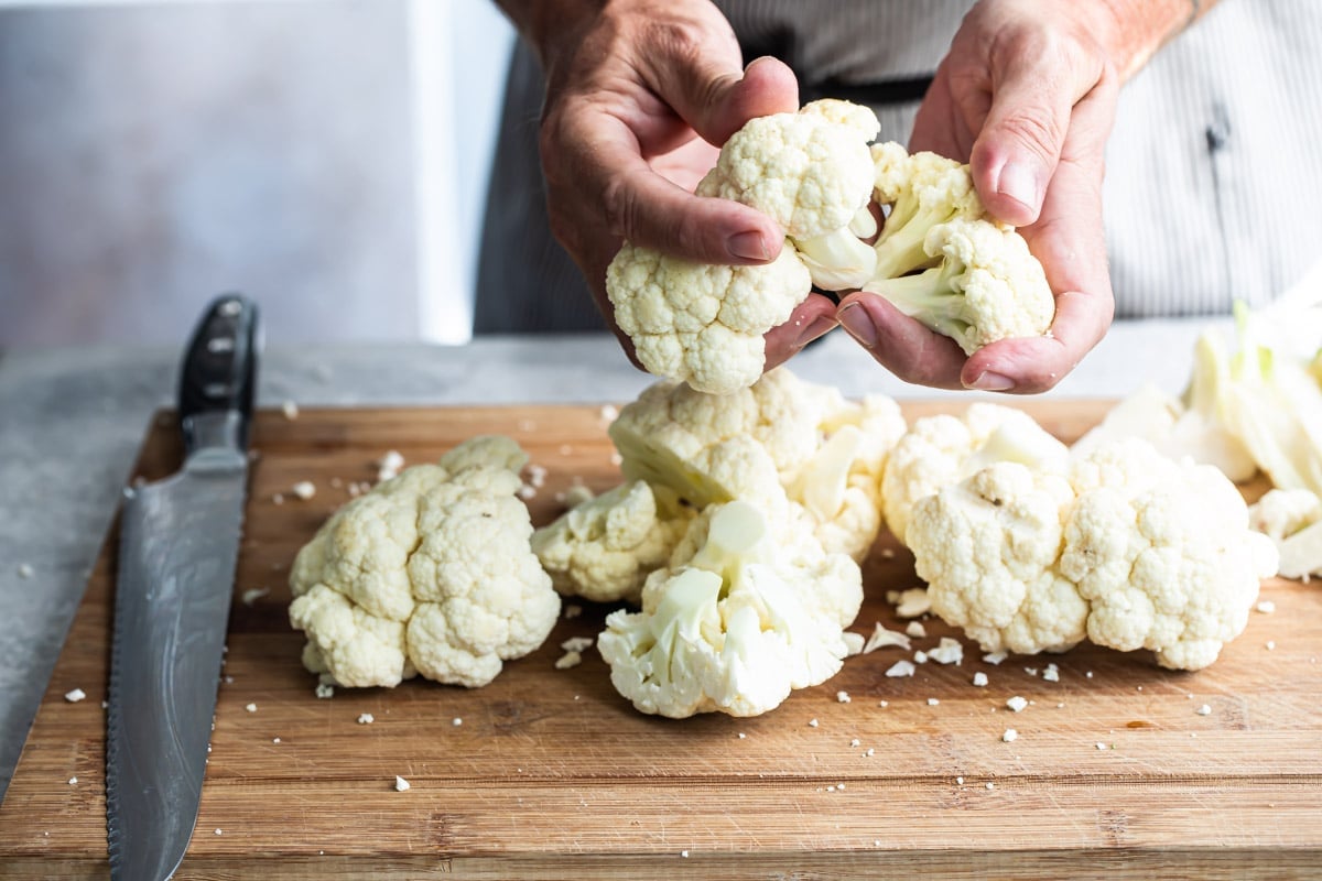 Raw cauliflower being chopped on a wooden cutting board.