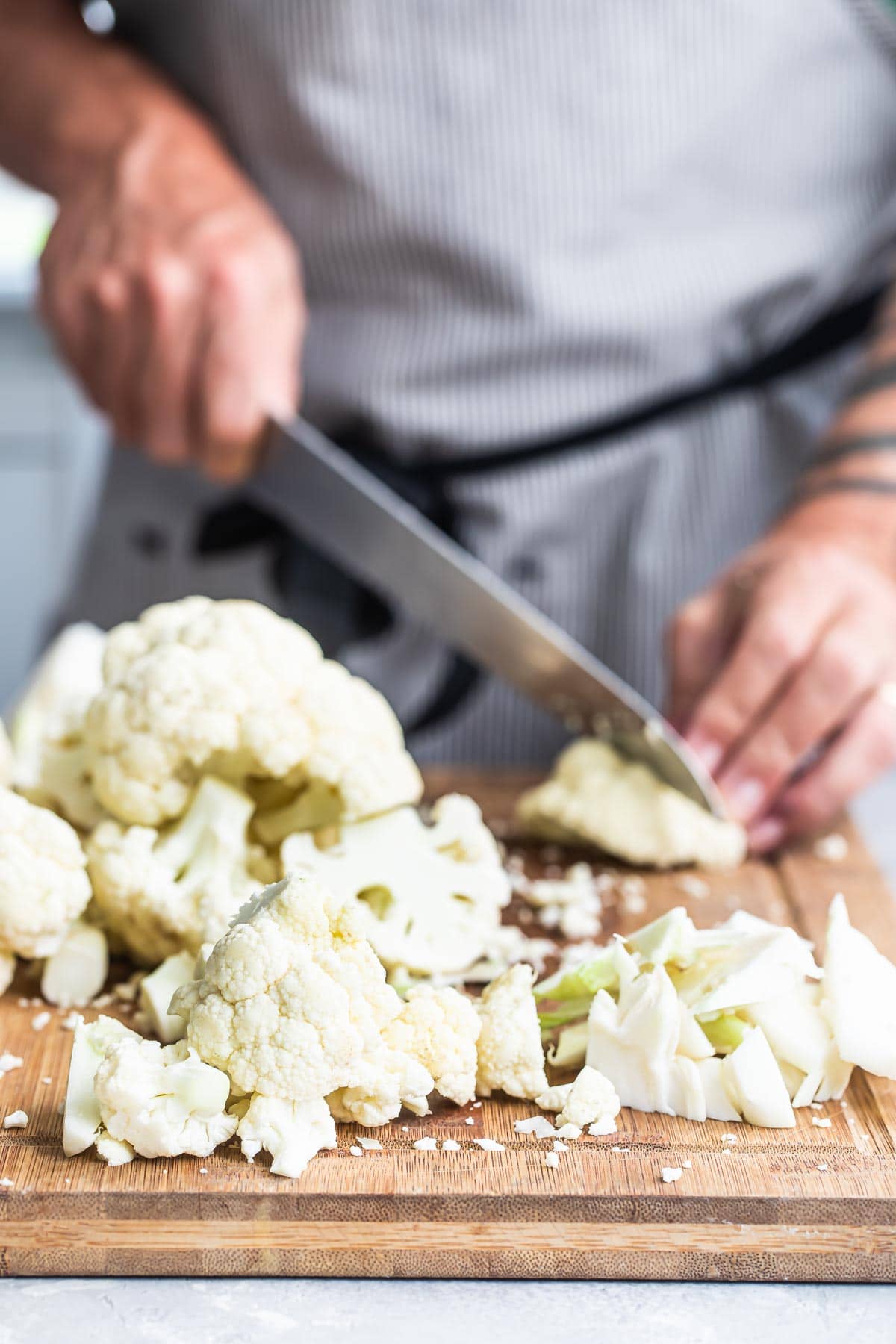 Raw cauliflower being chopped on a wooden cutting board.