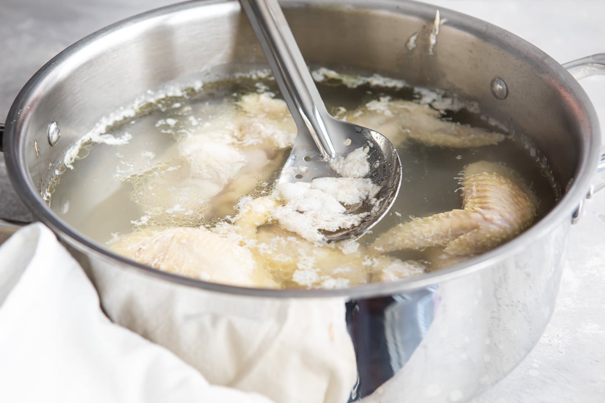 Fat being scooped off the top of chicken broth in a silver pot.
