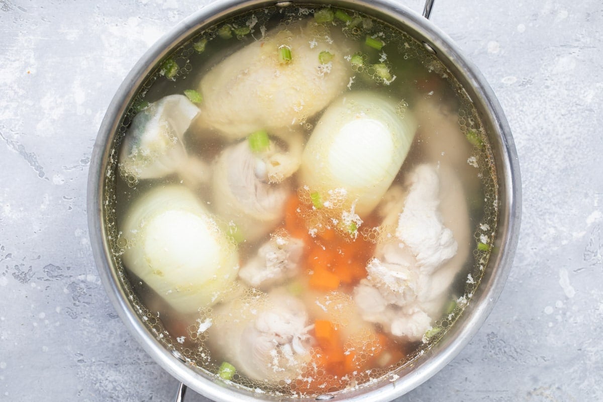 Chicken broth ingredients in water in a silver pot.