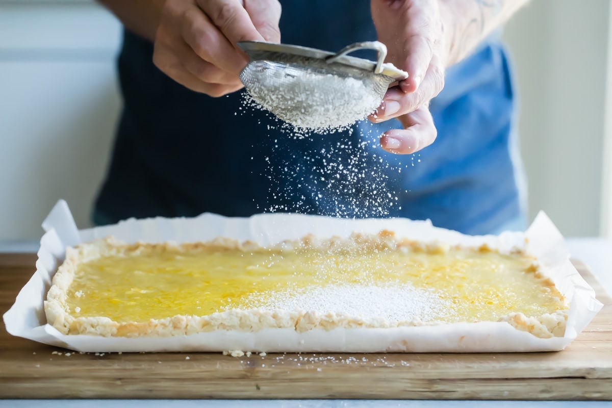 Someone sprinkling powdered sugar over lemon bars.