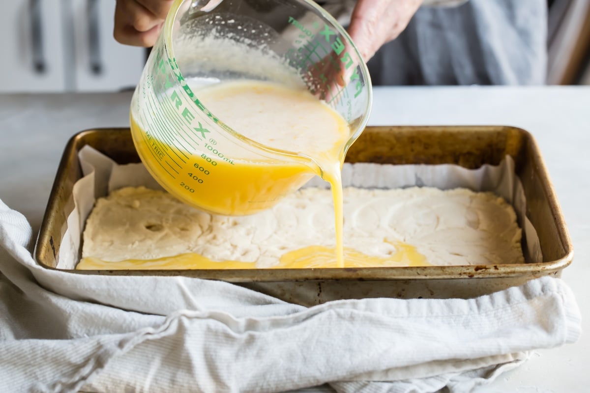 Someone pouring lemon mixture onto the crust for lemon bars.