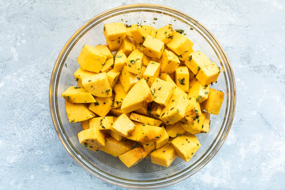 Raw cubed butternut squash in a bowl with olive oil and fresh thyme.
