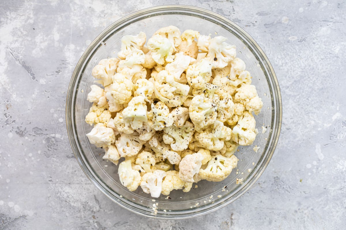 Cauliflower in a clear bowl coated with oil and seasonings.