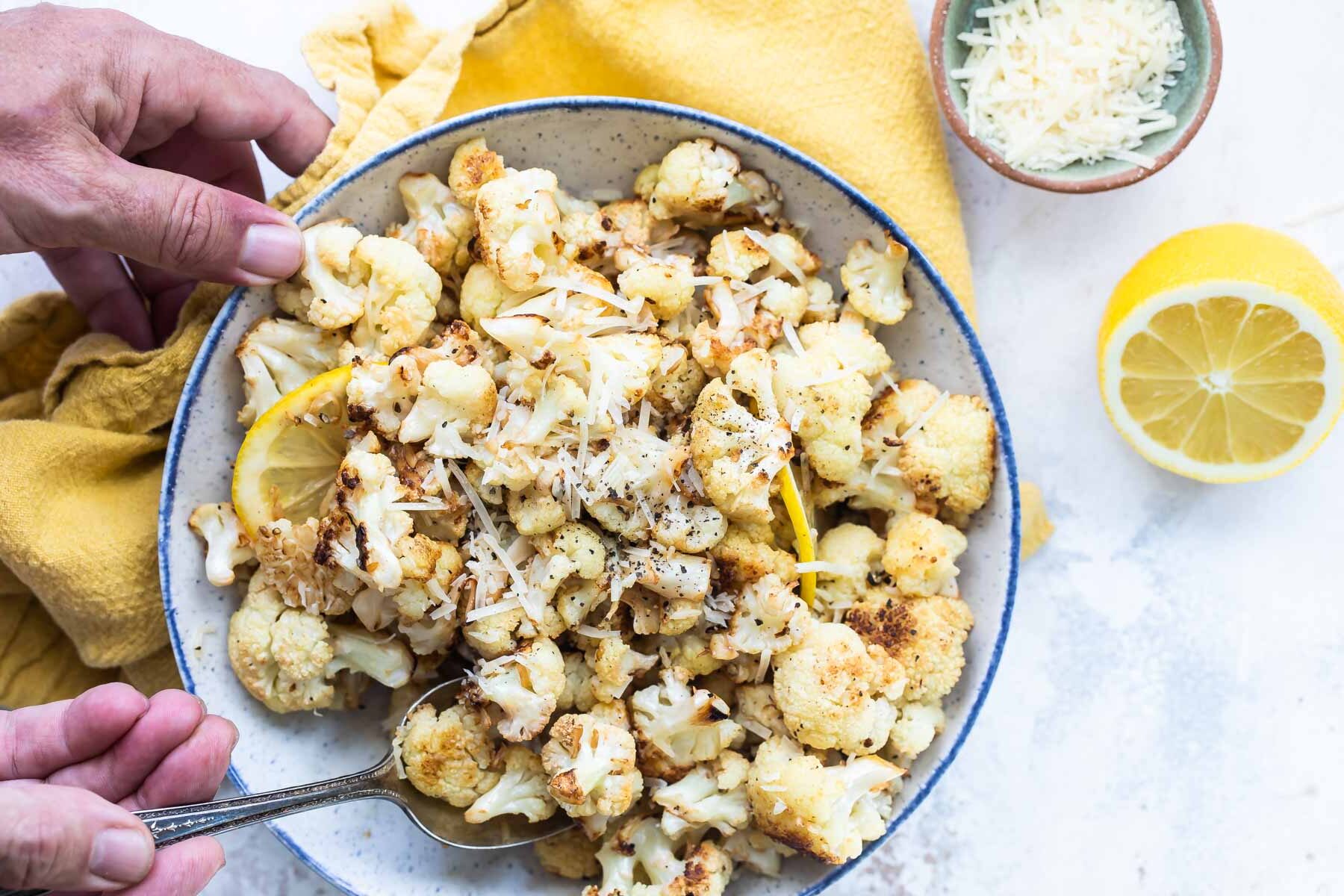 Someone scooping a spoonful of roasted cauliflower out of a white bowl.