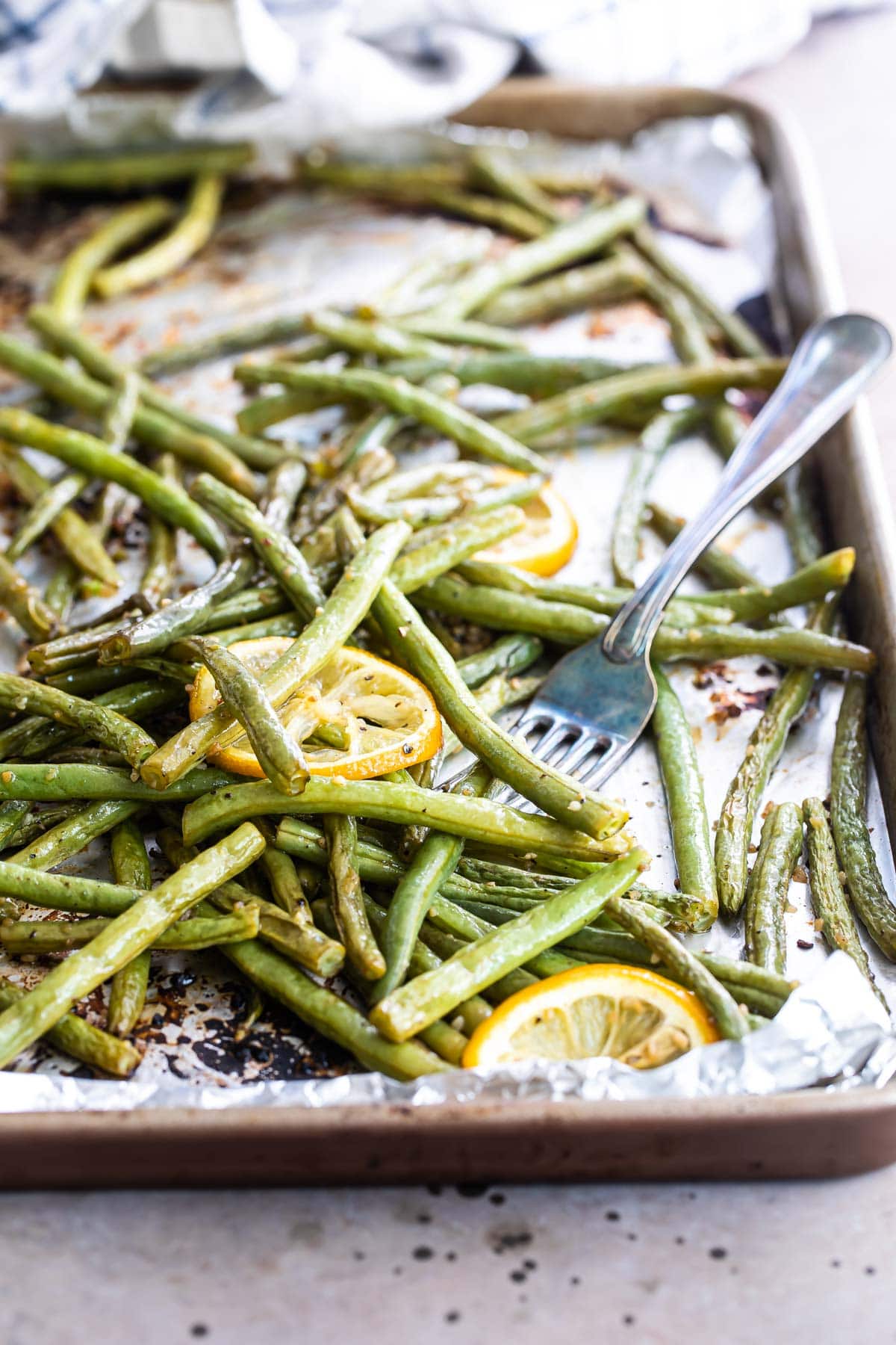 Roasted green beans on a baking sheet with lemon garnish.