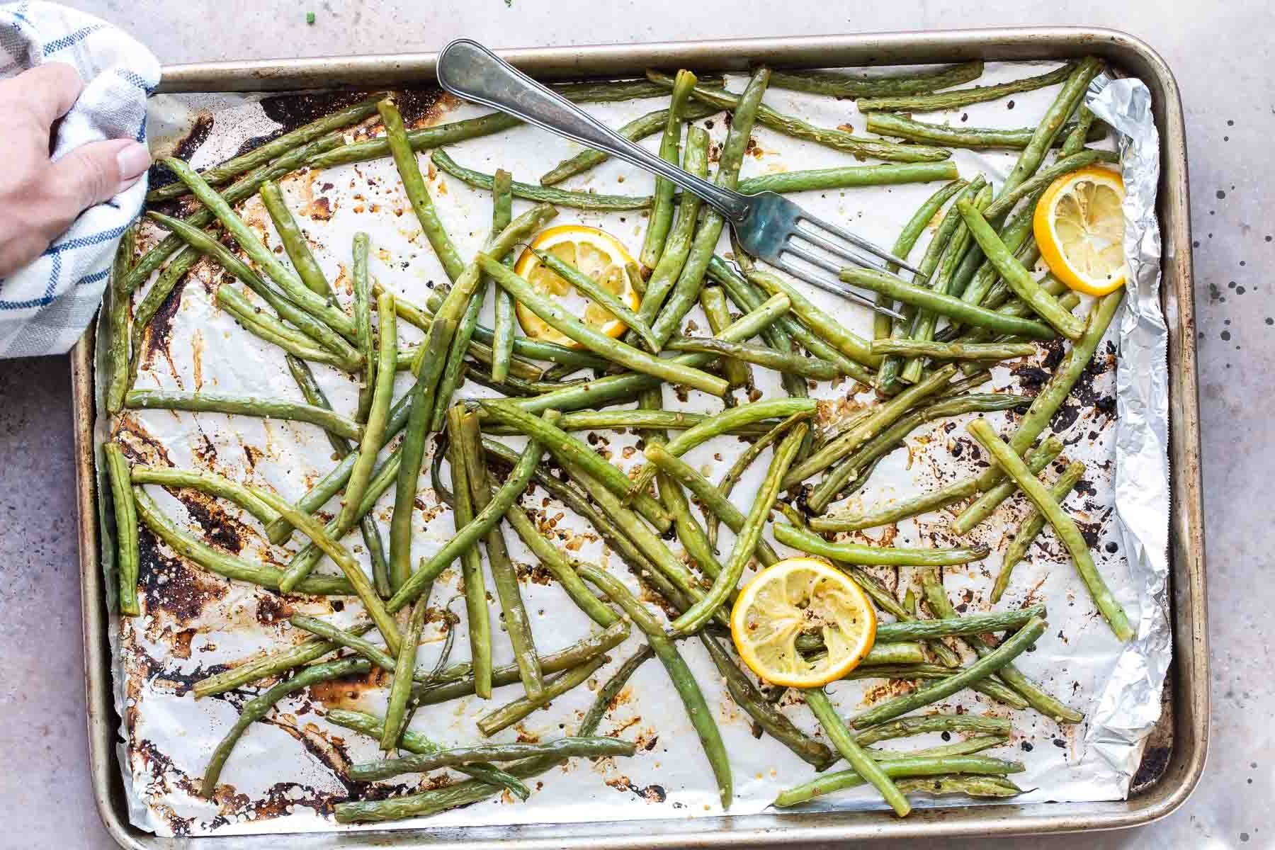 Roasted green beans on a baking sheet with lemon garnish.