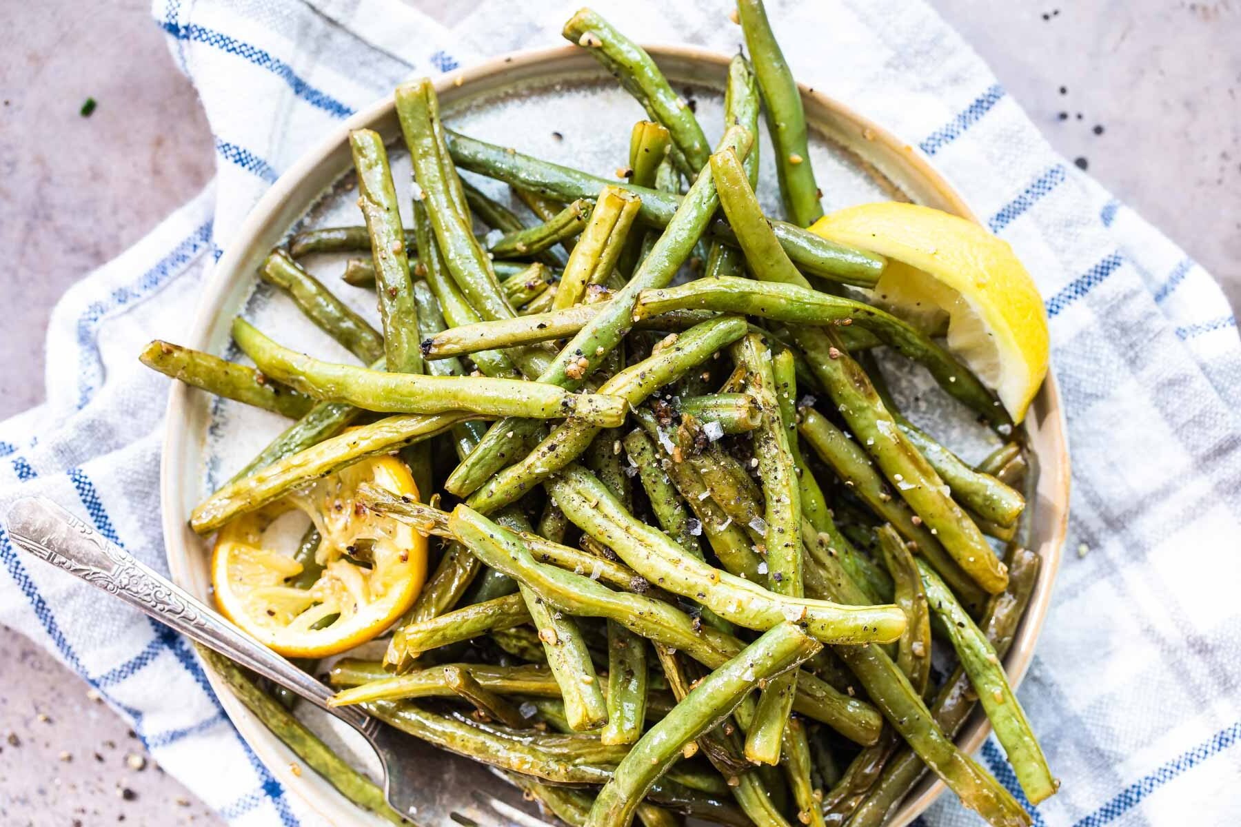 Roasted green beans on a round platter with lemon garnish.