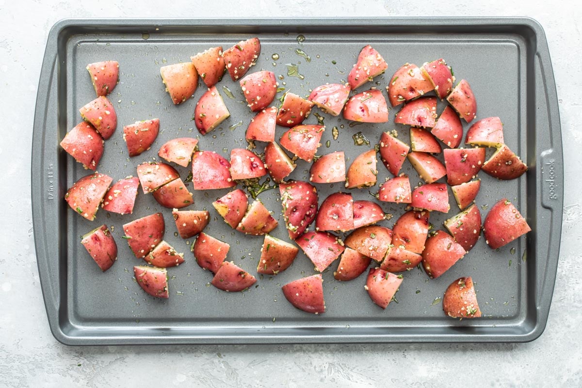 Red potatoes with seasoning on a baking sheet.