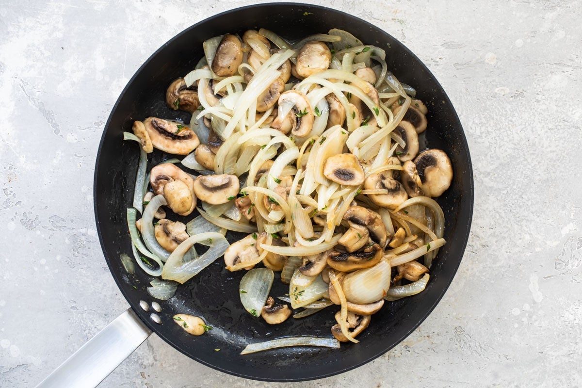 Mushrooms and onions cooking in a skillet.