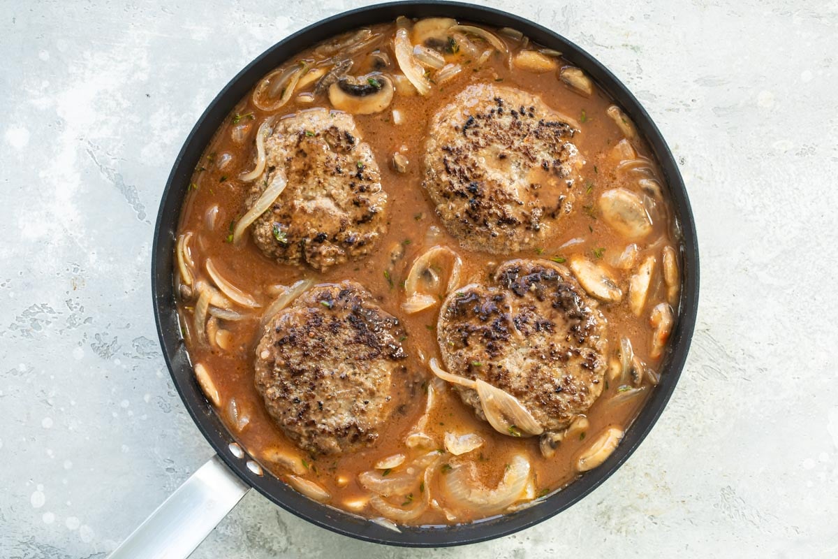 Salisbury steaks in a skillet with mushrooms, onions, and gravy.