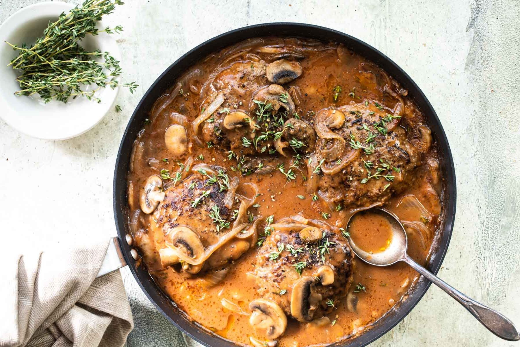 Salisbury steaks in a skillet with mushrooms, onions, and gravy.