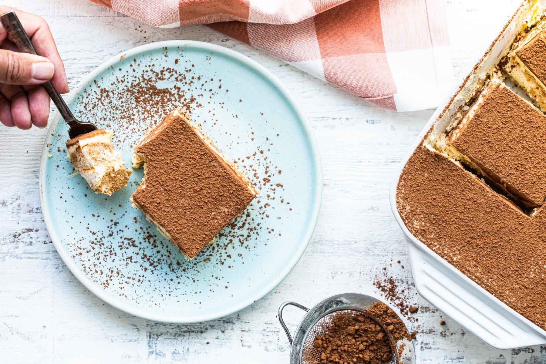 A piece of tiramisu on a blue plate with a fork.