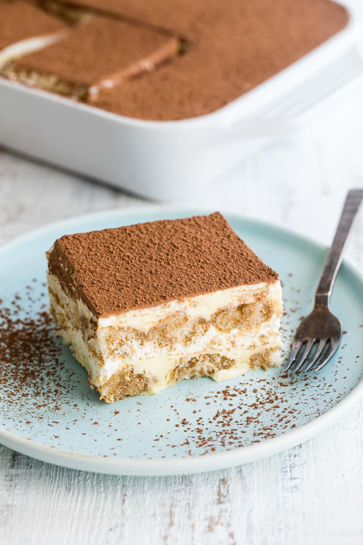 A piece of tiramisu on a blue plate with a fork.