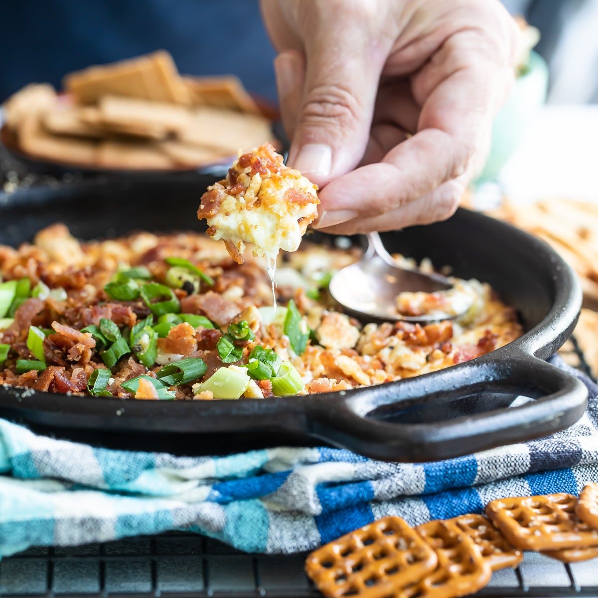 Cheesy bacon dip being scooped out of a cast iron skillet.