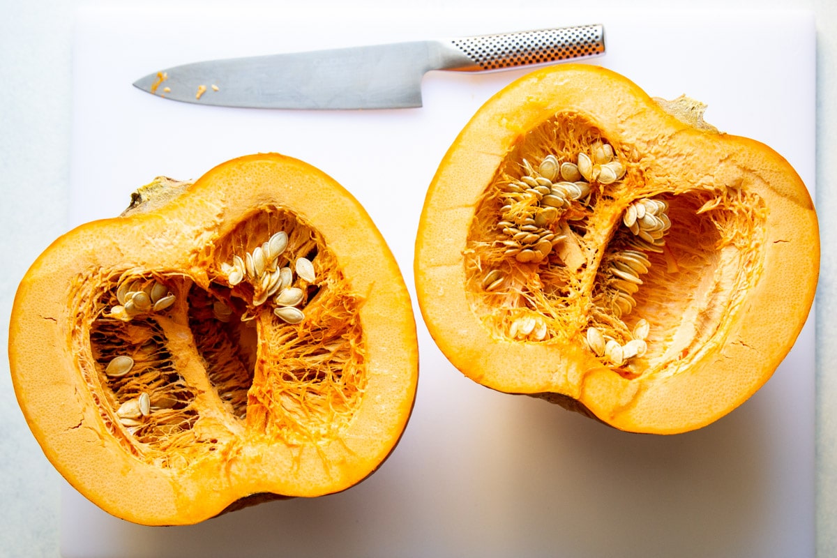 A pumpkin cut in half on a cutting board.