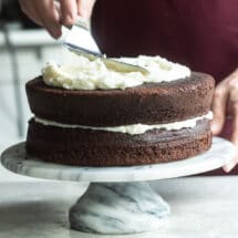 Buttercream frosting being spread on a chocolate layer cake.