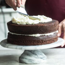 Buttercream frosting being spread on a chocolate layer cake.