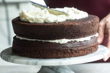Buttercream frosting being spread on a chocolate layer cake.