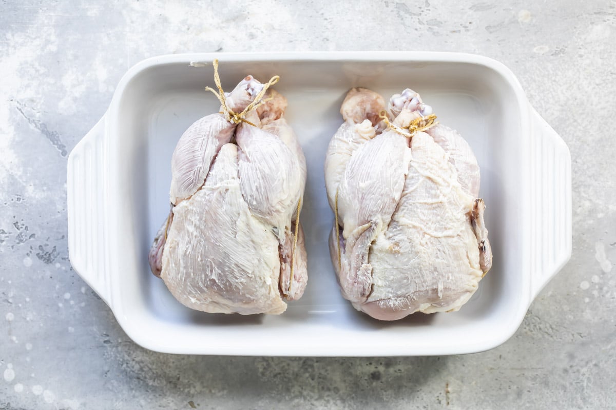 Two unbaked Cornish hens in a baking dish.