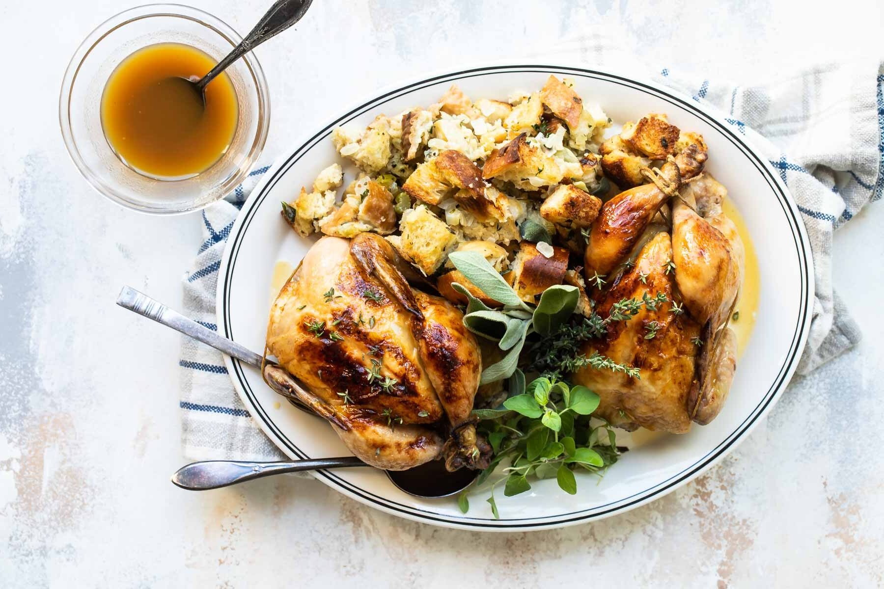Two whole Cornish hens on a gray plate with stuffing.