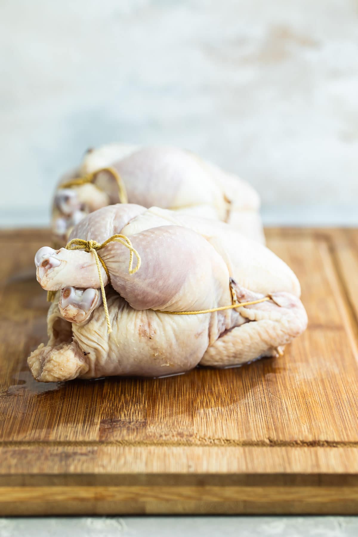 Two trussed Cornish hens on a wooden cutting board.