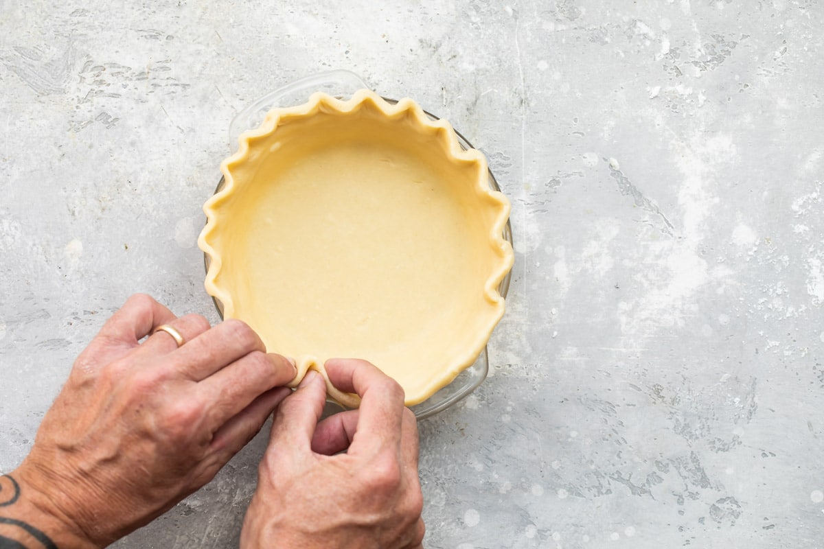 A mini pumpkin pie crust being crimped on the top edge.