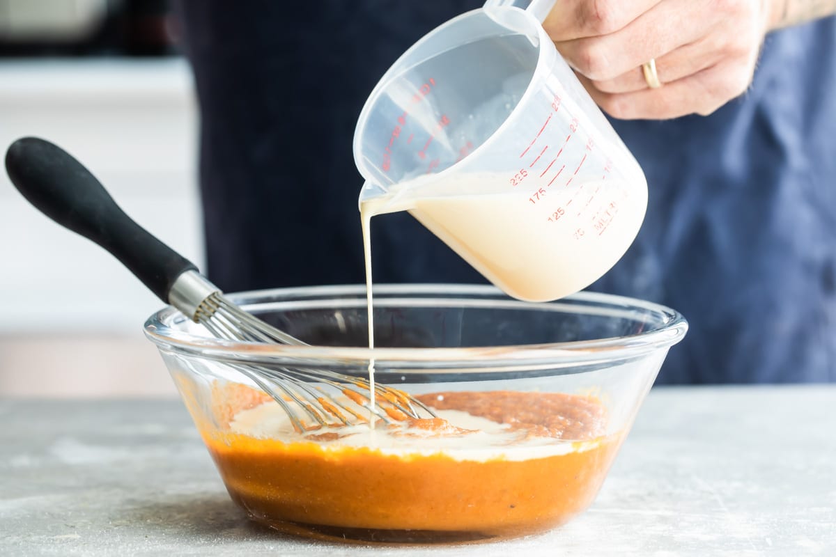 White liquid being poured into a clear bowl with pumpkin puree.