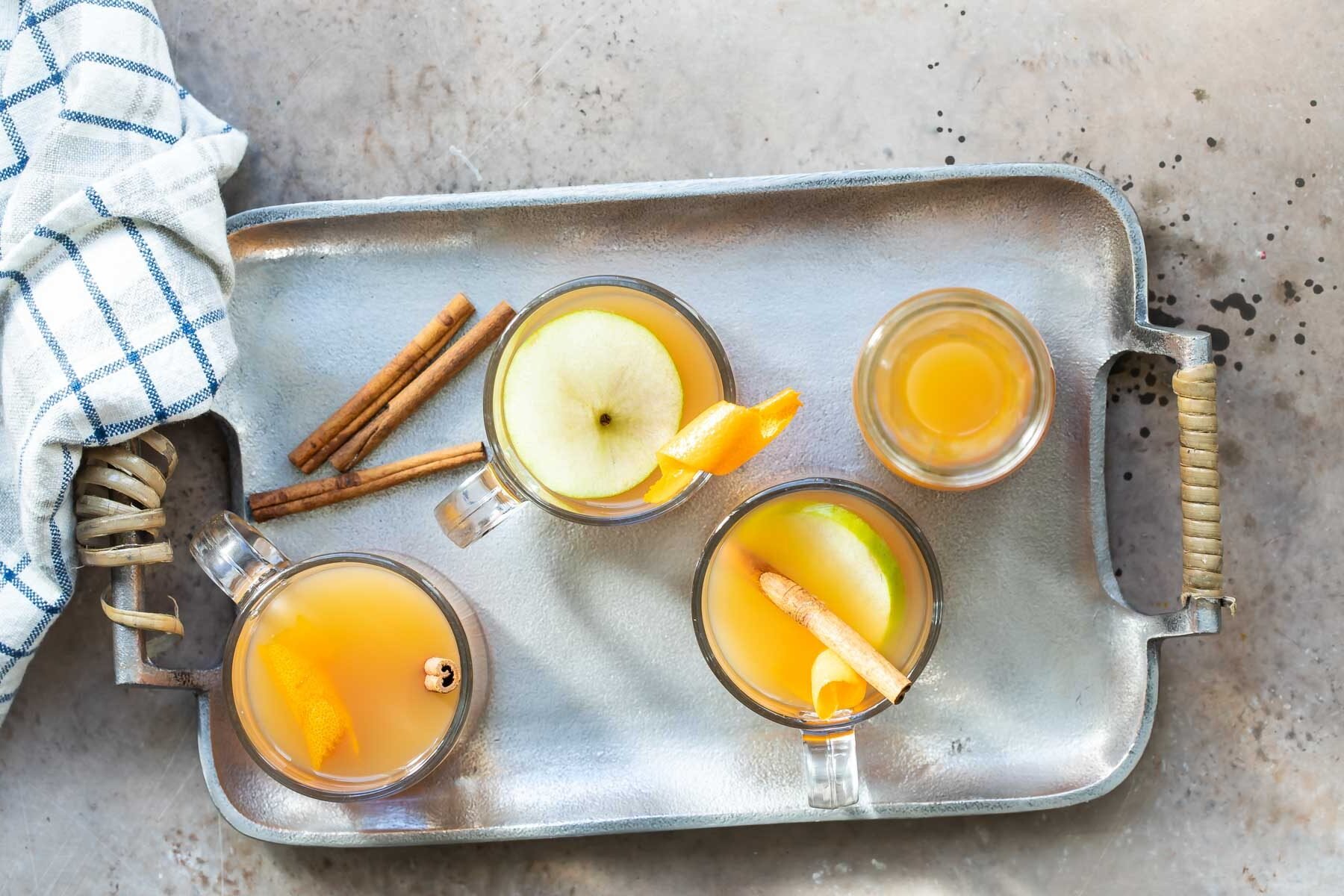 Three glasses and a carafe of mulled cider on a silver serving platter.