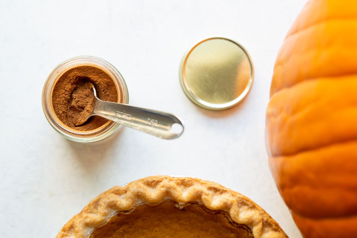 Pumpkin pie spice in a jar next to a pumpkin pie.