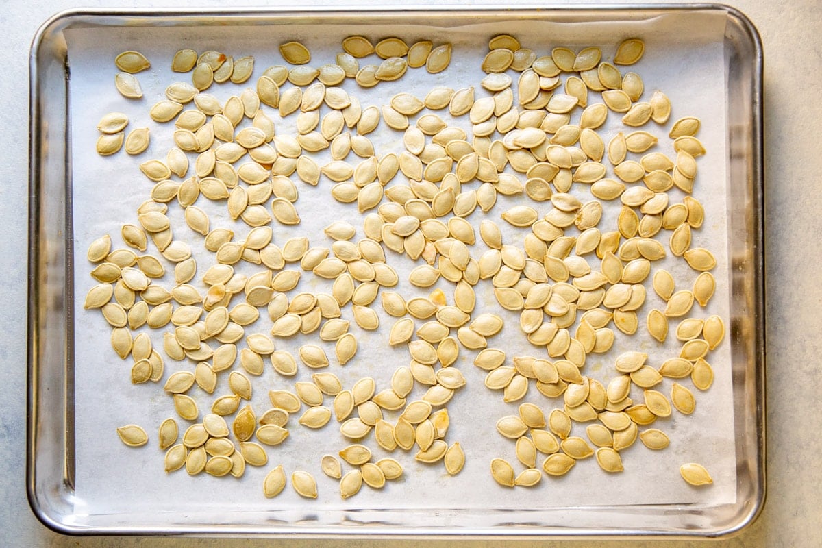 Pumpkin seeds on top of parchment paper on a baking sheet.