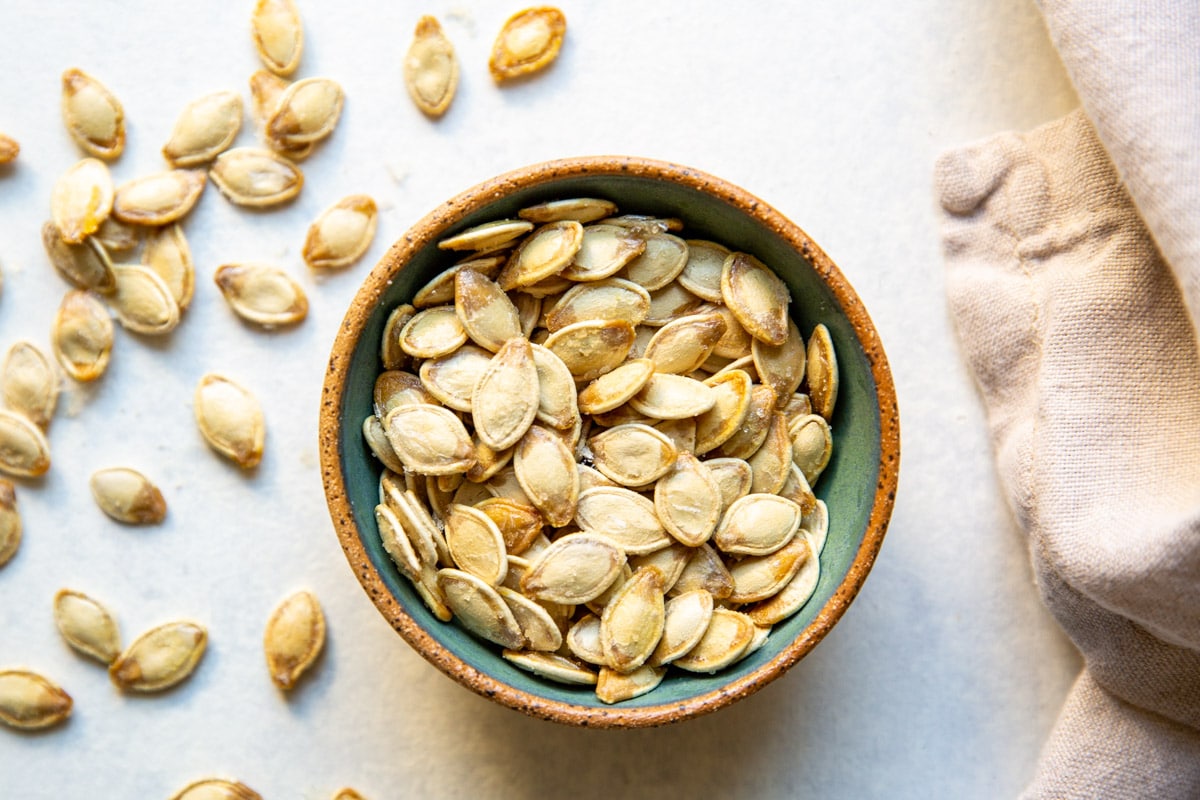 Roasted pumpkin seeds in a brown and teal bowl.