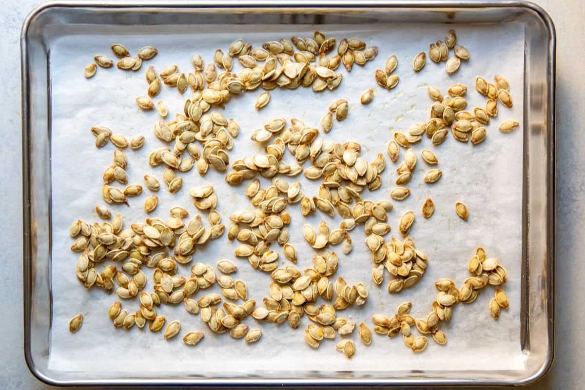 Pumpkin seeds on top of parchment paper on a baking sheet.