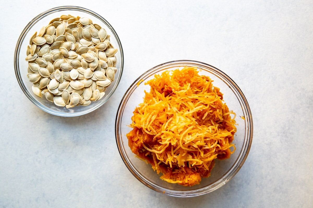 Pumpkin puree in a clear bowl next to pumpkin seeds in a clear bowl.