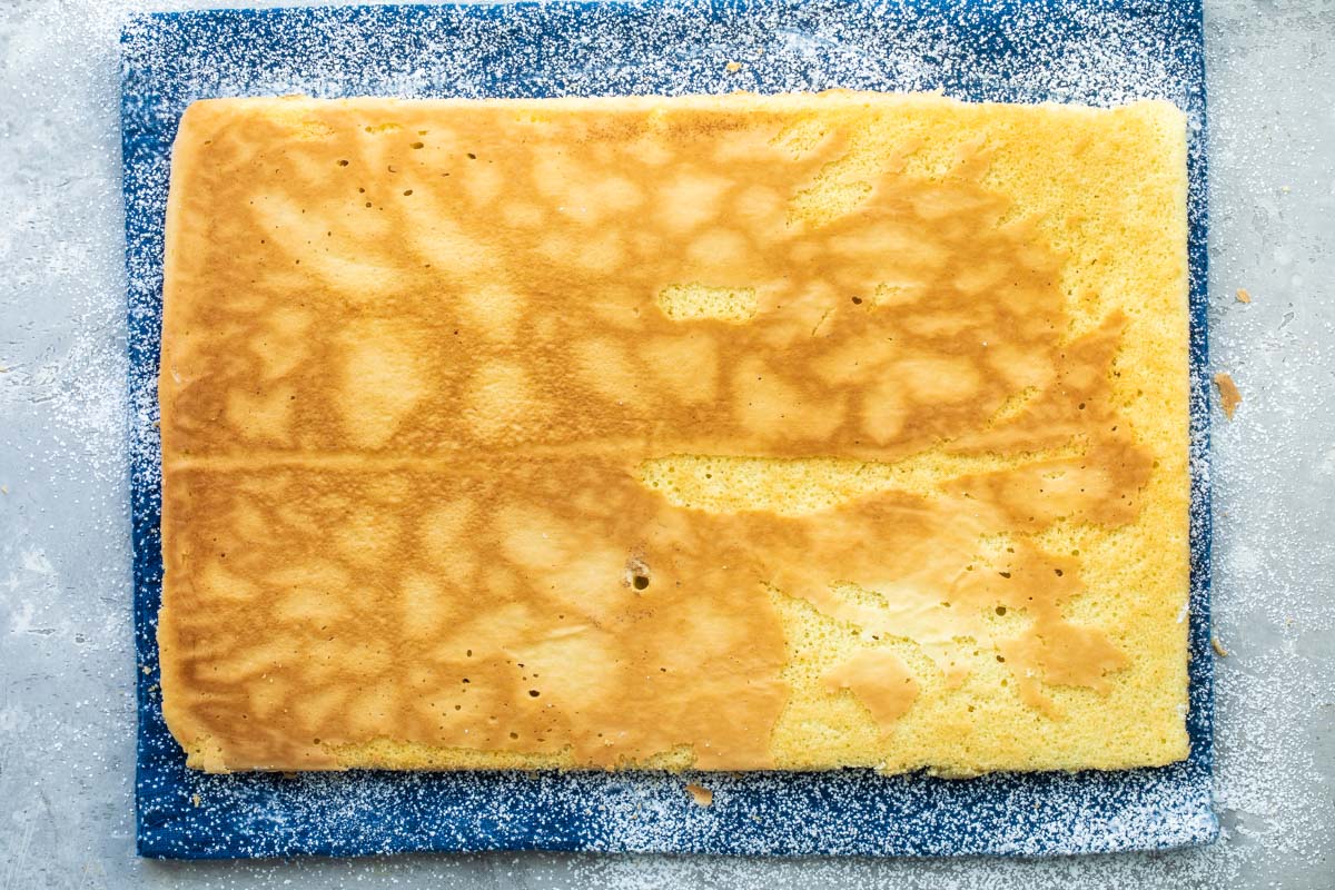 A baked roll cake lying flat on a kitchen towel before being rolled.