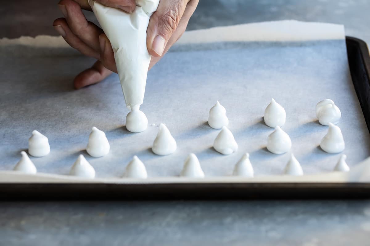 Meringue mushrooms piped on a baking sheet.