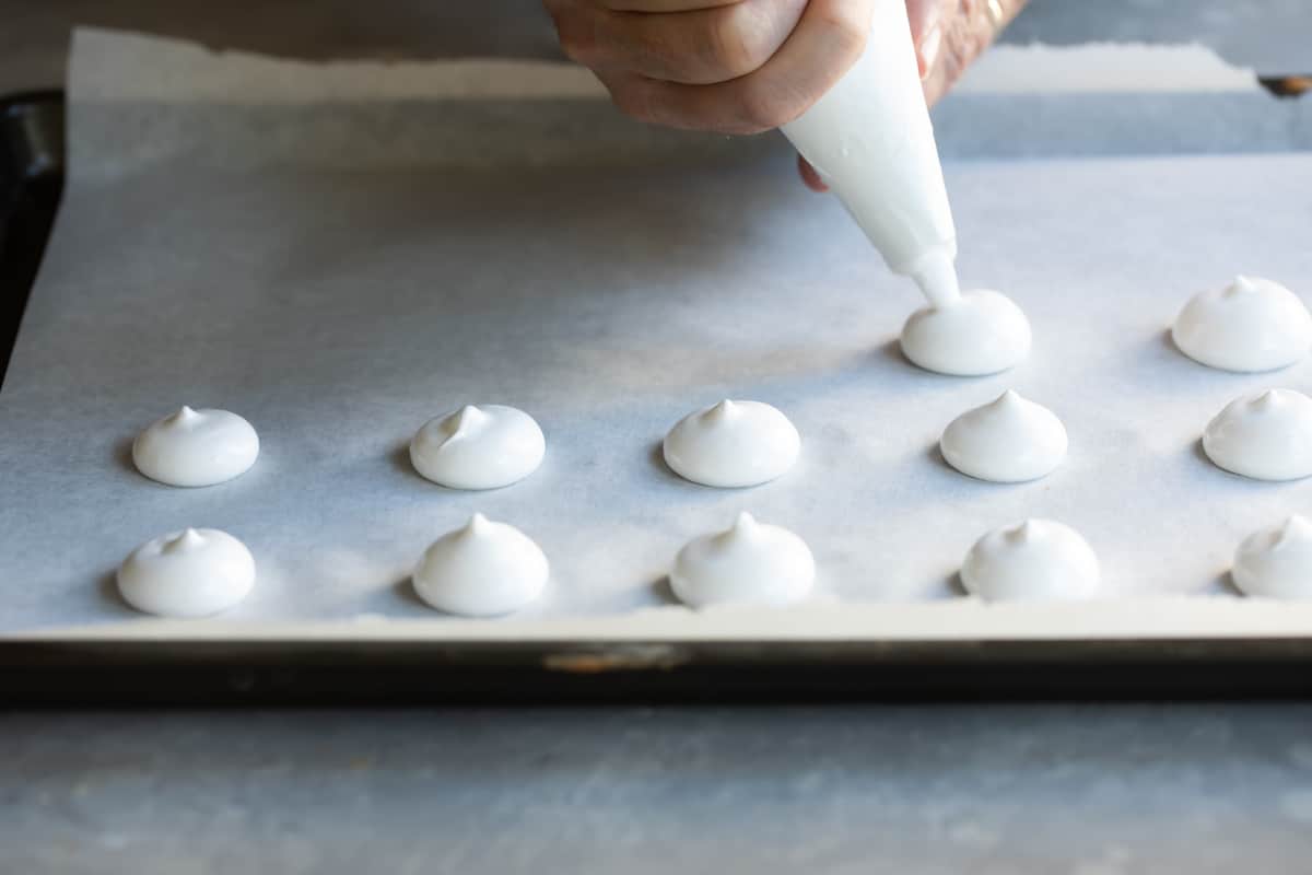 Meringue mushrooms piped on a baking sheet.