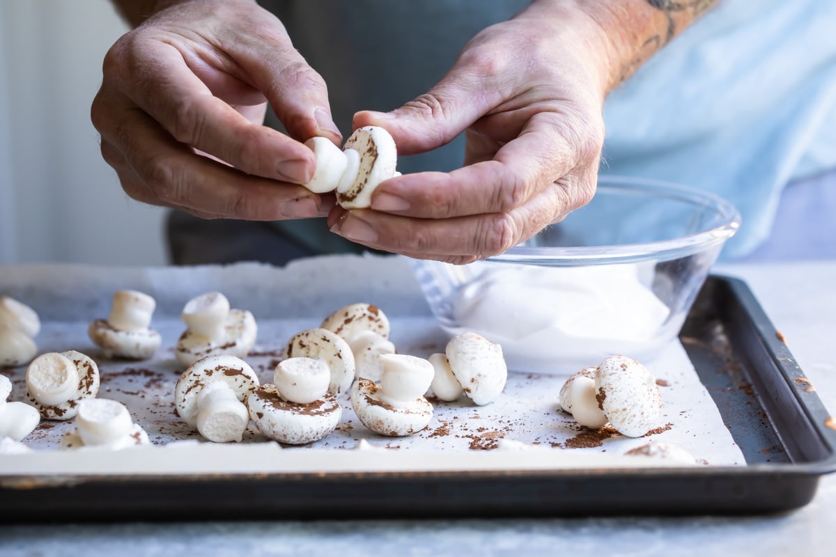 Meringue mushrooms piped on a baking sheet.
