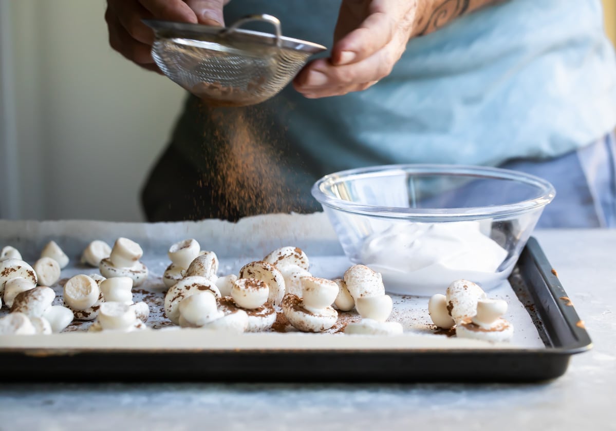 Meringue mushrooms piped on a baking sheet.