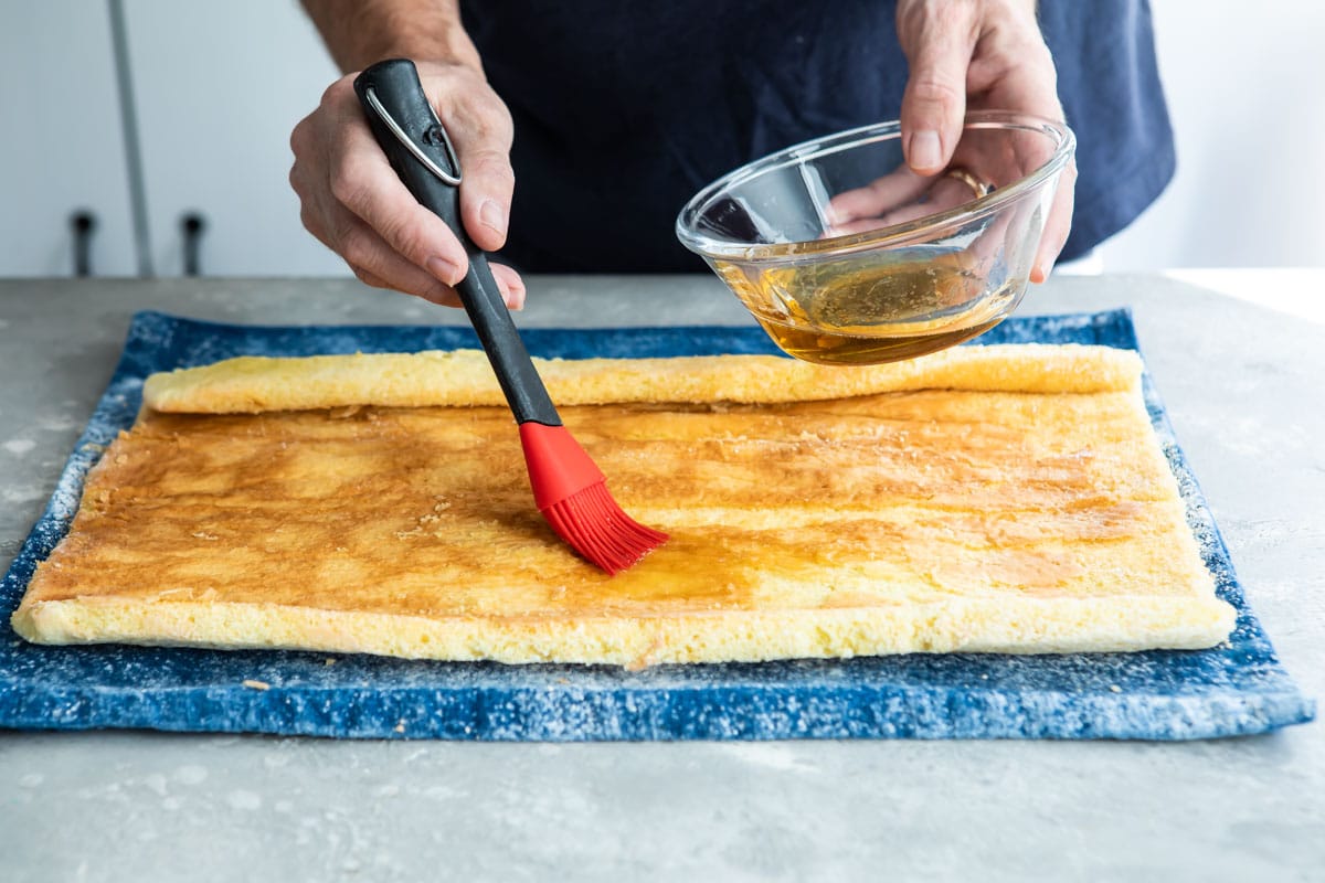 Rum syrup being brushed over a roll cake.