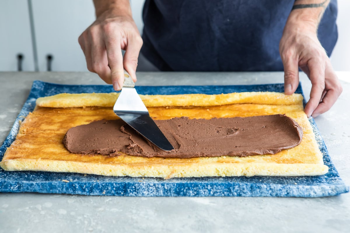 Chocolate frosting being spread over a roll cake.