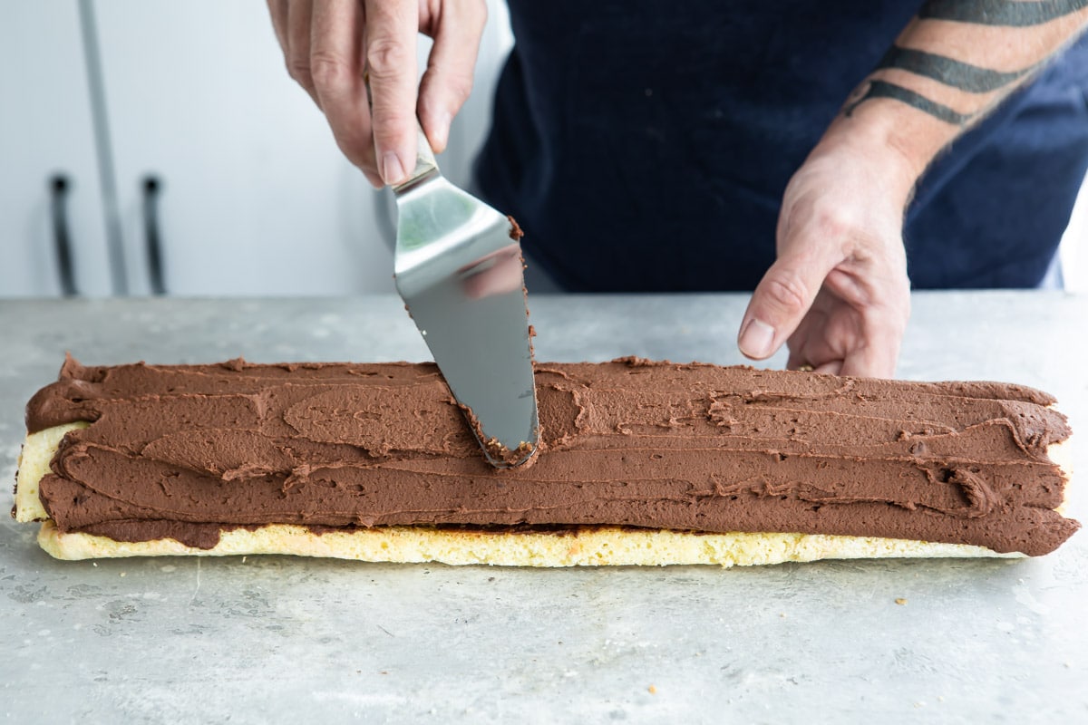 Chocolate frosting being spread over a roll cake.