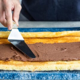 Chocolate frosting being spread over a roll cake.