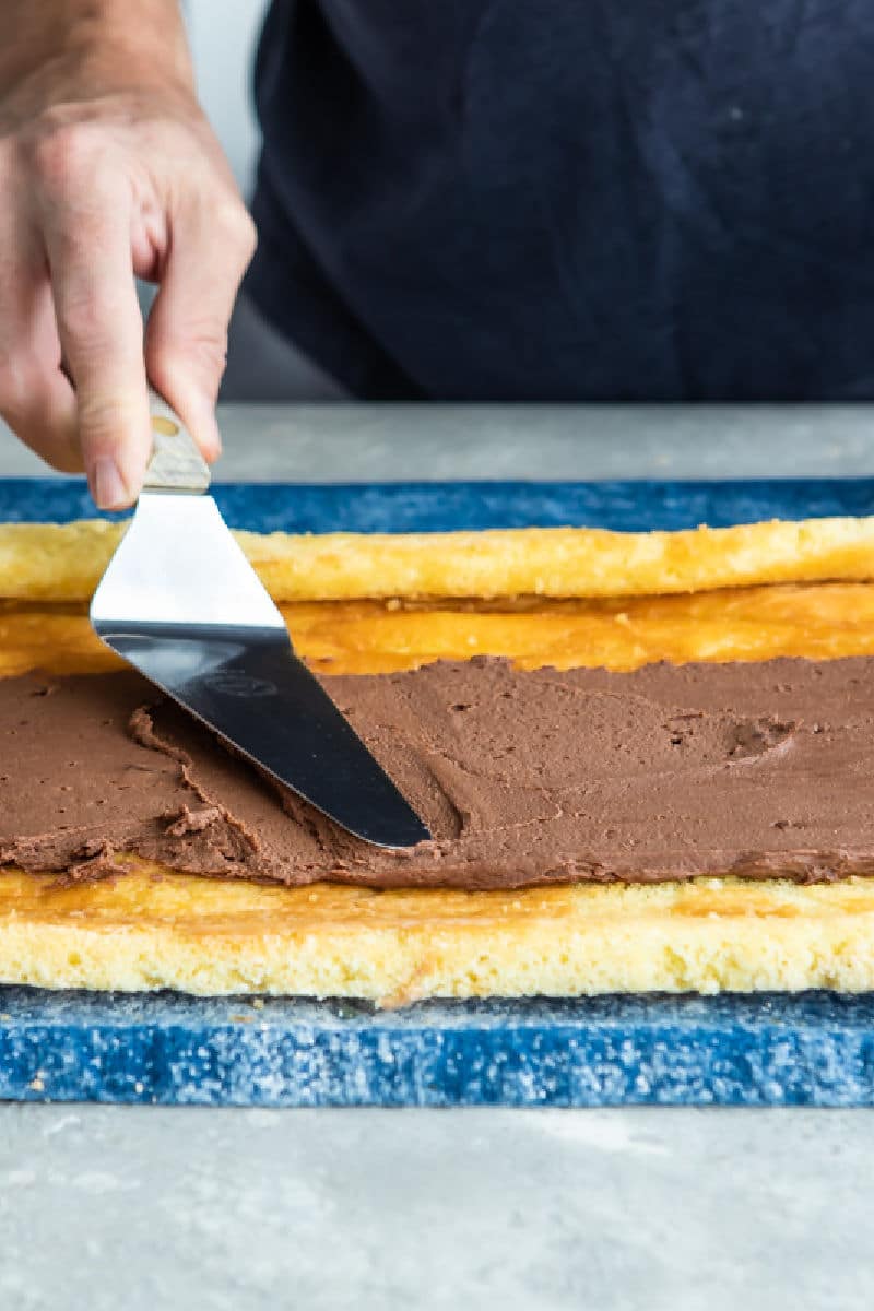 Chocolate frosting being spread over a roll cake.