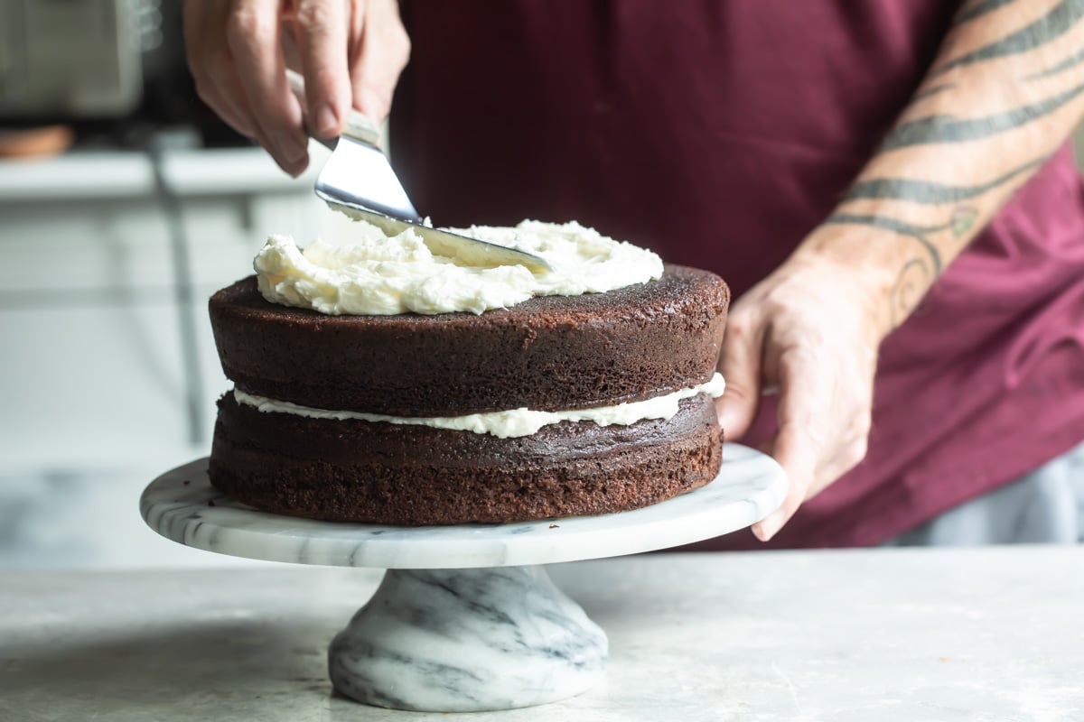 Someone spreading frosting on a chocolate cake.