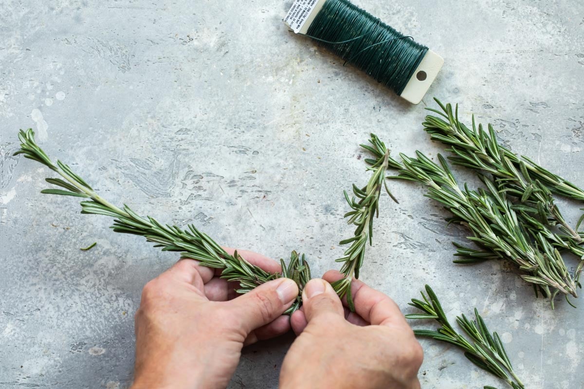 Someone forming a wreath out of rosemary with floral wire.