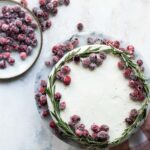 A cranberry wreath cake on a granite cake platter with a small plate of sugared cranberries next to it.
